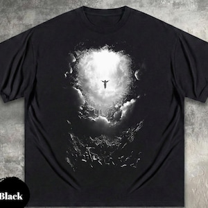 May include: Black t-shirt featuring a grayscale graphic of a person with outstretched arms against a bright, cloudy background. The design evokes a sense of freedom and spirituality. The word "Black" is printed on a black circle.