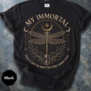 May include: A black t-shirt featuring a gold-toned graphic of a dragonfly centered above an hourglass. The text reads MY IMMORTAL and There's just too much that time cannot erase. The design includes celestial elements like a crescent moon and stars.