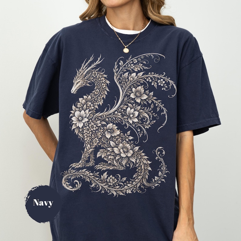 May include: A navy blue short-sleeve t-shirt featuring a large, intricate graphic of a dragon composed entirely of detailed floral patterns and leaves in shades of cream and light gray. The design covers the center of the chest area.