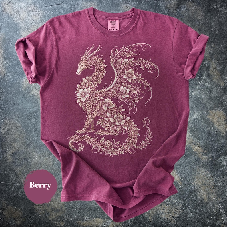 May include: A berry-colored short-sleeve t-shirt featuring a cream-colored graphic of a dragon composed entirely of intricate floral patterns and vines. The shirt has a crew neckline and a small tag at the collar that reads Comfort Colors.