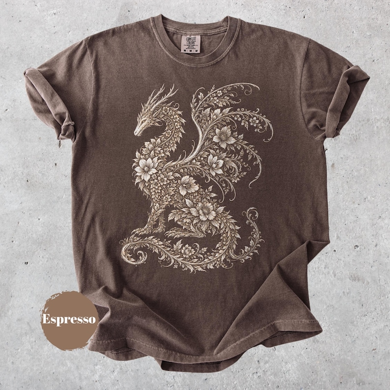 May include: A brown short-sleeve t-shirt featuring a large, intricate graphic of a dragon composed entirely of floral and vine patterns in a light beige color. The shirt has a crew neckline and a small label at the inner collar. The word Espresso is visible.