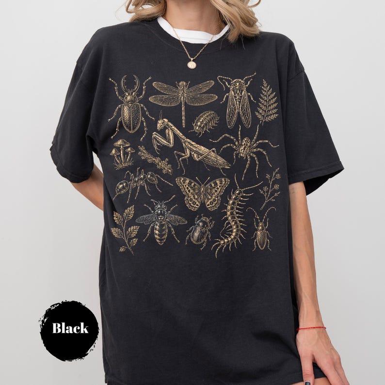 May include: A black short-sleeved t-shirt featuring a gold-toned graphic print of various insects, including a praying mantis, butterfly, dragonfly, beetle, and centipede, alongside small botanical elements like mushrooms and fern leaves.
