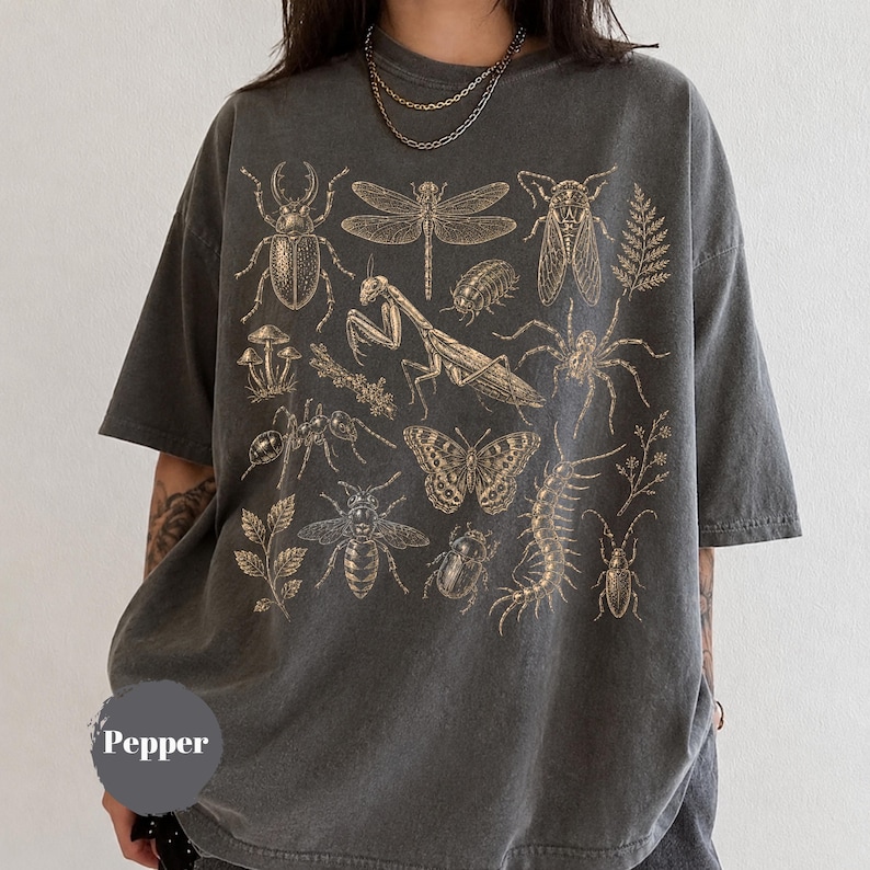 May include: A charcoal gray short-sleeve t-shirt featuring a gold-toned graphic print of various insects, including a praying mantis, dragonfly, beetle, and butterfly, alongside botanical elements. The word Pepper is printed in a gray circle.