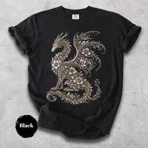 May include: A black short-sleeve t-shirt featuring a large, intricate graphic of a dragon composed entirely of detailed floral patterns and swirling vines in shades of cream and light beige, centered on the front of the garment.