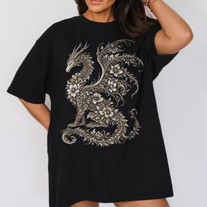 May include: A black t-shirt featuring a large, intricate graphic print of a dragon composed entirely of detailed floral patterns and swirling vines in shades of cream and light gray, centered on the front of the garment.