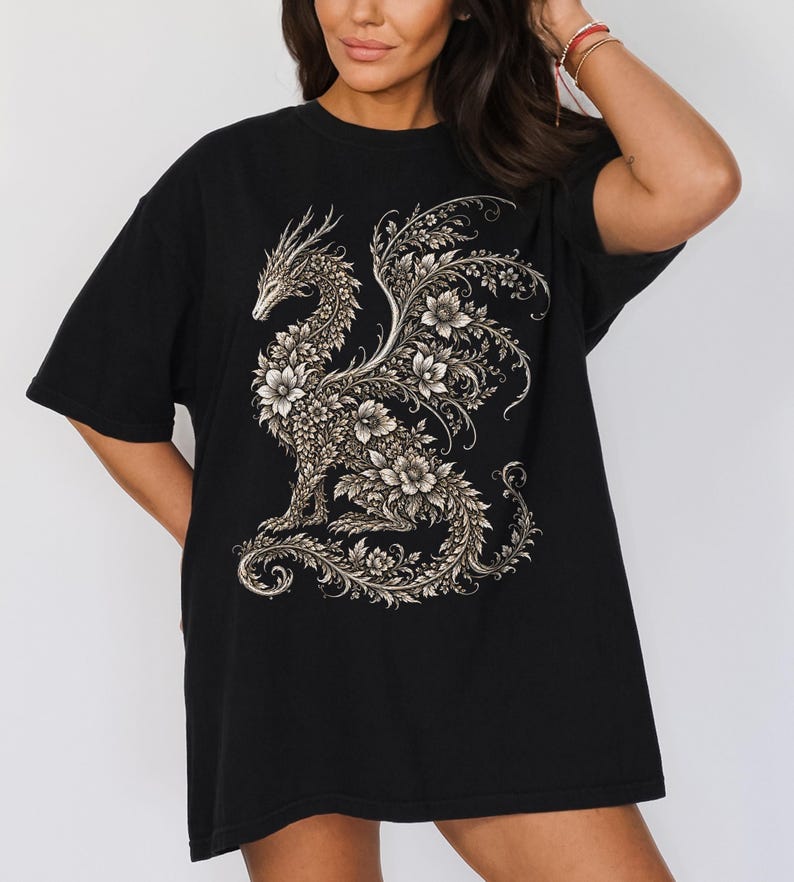 May include: A black t-shirt featuring a large, intricate graphic print of a dragon composed entirely of detailed floral patterns and swirling vines in shades of cream and light gray, centered on the front of the garment.