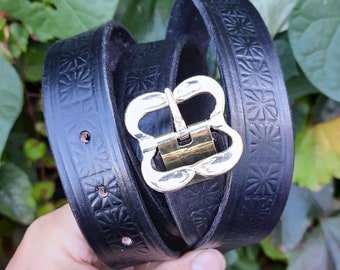 May include: Black leather belt with a gold metal buckle. The belt has a floral pattern embossed into the leather.