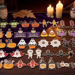 May include: A collection of colorful Halloween-themed metal charms featuring various designs including pumpkins, ghosts, bats, mummies, spiders, witches, and candy corn. Each charm has a small loop at the top for attachment, showcasing detailed enamel work.