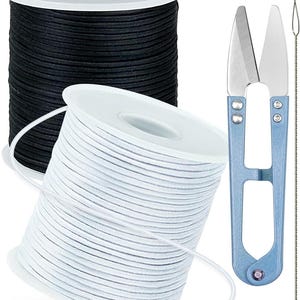 Op de afbeelding: Twee klossen koord, een zwarte en een witte, vergezeld van een lichtblauwe metalen draadschaar en een dunne draad-inrijger. De klossen zijn cilindervormig met witte kunststof uiteinden en de schaar heeft scherpe, puntige stalen bladen.