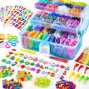 May include: A multi-tiered clear plastic storage case filled with colorful rubber bands, accompanied by sheets of number and letter stickers, various plastic charms, small plastic hooks, colorful beads, and several tassels for crafting projects.