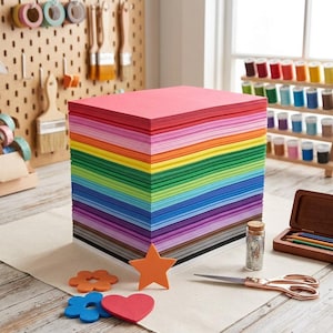 May include: A large stack of rectangular craft foam sheets in a rainbow of colors, including red, orange, yellow, green, blue, purple, gray, and white. Several small foam cutouts in star, heart, and flower shapes are placed in front of the stack.