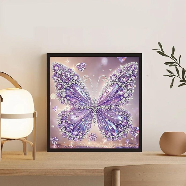 Puede incluir: Una pieza de arte mural cuadrada y enmarcada que presenta un motivo central de mariposa en tonos violeta y lavanda. La mariposa est&aacute; adornada con numerosas gemas circulares reflectantes que crean una apariencia brillante y texturizada.