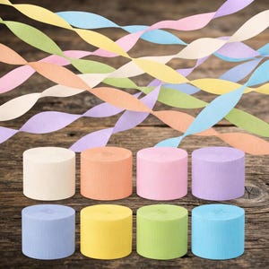 May include: Eight cylindrical rolls of crepe paper in pastel shades of cream, peach, pink, lavender, light blue, yellow, lime green, and sky blue, with matching twisted paper streamers draped in the background above the rolls.