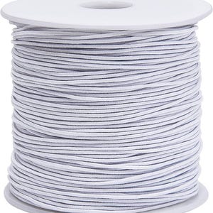 May include: A spool of white elastic cord wrapped neatly around a white plastic reel. The thin, flexible cord is wound in multiple horizontal layers, creating a uniform cylindrical shape with a smooth texture and a consistent bright white color.