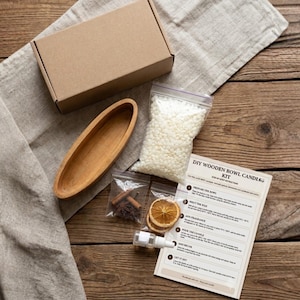 May include: A DIY wooden bowl candle kit including a brown cardboard box, an oval wooden bowl, a bag of white wax pellets, a small bottle of fragrance, dried orange slices, star anise, cinnamon sticks, and an instruction sheet with text.