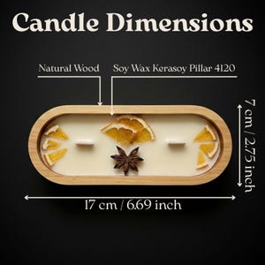 May include: An oval candle in a natural wood container with soy wax, two wooden wicks, dried orange slices, and a star anise. Text reads Candle Dimensions, Natural Wood, Soy Wax Kerasoy Pillar 4120, 7 cm / 2.75 inches, and 17 cm / 6.69 inches.