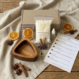 May include: A DIY wooden bowl candle kit containing a brown cardboard box, a triangular wooden bowl, a bag of white wax pellets, a small bottle of fragrance, a metal wick base, cinnamon sticks, star anise, dried orange slices, and instructions.