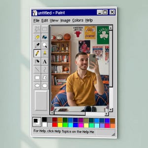 Può includere: Un'opera d'arte incorniciata progettata per assomigliare alla classica interfaccia del programma Paint di Windows. L'opera presenta un selfie di una persona con una polo giallo senape. Lo sfondo include palloni da basket, poster e una libreria. Il testo "untitled - Paint" è visibile.