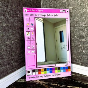 Puede incluir: Un espejo con marco rosa dise&ntilde;ado para parecerse a la cl&aacute;sica aplicaci&oacute;n Paint de Windows. El espejo presenta la barra de t&iacute;tulo "untitled - Paint", opciones de men&uacute; y una paleta de colores en la parte inferior. El reflejo muestra una habitaci&oacute;n con una puerta.