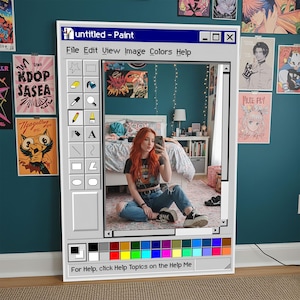 Può includere: Un grande specchio rettangolare progettato per assomigliare all'interfaccia del programma Windows Paint classico. La cornice dello specchio è bianca, con una barra degli strumenti di icone a sinistra e una tavolozza di colori in basso. Lo specchio riflette una stanza con poster e una persona.