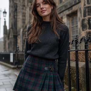 May include: A dark gray sweater paired with a green, navy, and red plaid pleated skirt. The skirt features a black leather belt with a silver buckle. The outfit is suitable for cooler weather and offers a classic, preppy style.