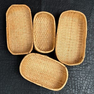 May include: Four light brown woven baskets with rounded corners and rectangular bases. The baskets feature a consistent, tight wicker weave pattern throughout the sides and bottoms, creating a uniform texture across all four individual storage containers.