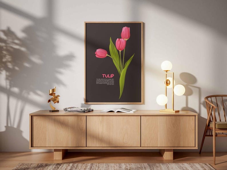 May include: A framed art print featuring three pink tulips with green leaves against a dark background. The word "TULIP" is displayed in pink. The print hangs above a wooden cabinet with a gold lamp and decorative items.