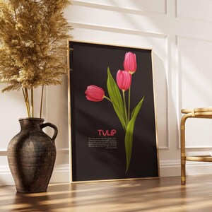 May include: A framed art print featuring three pink tulips with green leaves against a black background. The word "TULIP" is displayed in pink text. The print is leaning against a white wall next to a decorative vase.