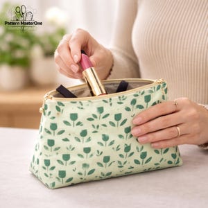 K&ouml;nnte beinhalten: Eine hellgr&uuml;ne Kosmetiktasche mit goldenem Rei&szlig;verschluss und einem Muster aus gr&uuml;nen tulpenartigen Formen. Eine Person h&auml;lt einen rosa Lippenstift und legt ihn in die Tasche. Die Tasche ist ge&ouml;ffnet und zeigt andere Kosmetikartikel.