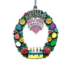 May include: A decorative ornament with a green wreath design, featuring colorful accents and a birthday cake. The ornament has a heart-shaped pendant with the word "Gymnastics" and the words "Happy Birthday" at the top.