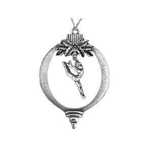 May include: Silver-toned ornament featuring a gymnast in a split pose within an oval frame. The frame has a textured surface and is topped with holly leaves and a decorative element. A loop is at the top for hanging.
