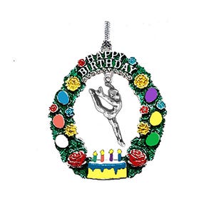 May include: A silver-toned gymnast charm hangs inside a green wreath with colorful accents. The wreath has the words "HAPPY BIRTHDAY" at the top. A yellow cake with candles is at the bottom.