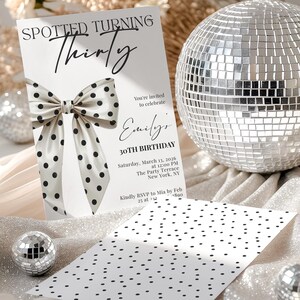 May include: A white birthday invitation card featuring a large black polka dot bow graphic and the text Spotted Turning Thirty, Emily's 30th Birthday, Saturday, March 13, 2026, at 12:00 PM, The Party Terrace, New York, NY. Includes a matching polka dot card.