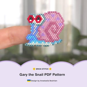 Op de afbeelding: Een geborduurd Gary the Snail-ontwerp in roze, blauw en rood, rustend op een vinger. Het ontwerp is een baksteekpatroon. De tekst "Gary the Snail PDF Pattern" is zichtbaar.