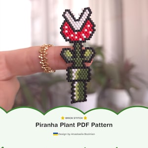 Könnte beinhalten: Ein pixeliges Piranha-Pflanzen-Design aus Perlen, mit einem rot-weißen Kopf, schwarzen Akzenten und einem grünen Stiel. Der Text "Piranha Plant PDF Pattern" ist zu sehen. Das Design erinnert an einen klassischen Videospielcharakter.
