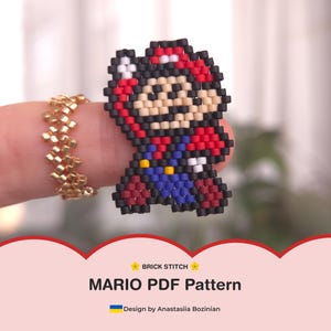May include: A beaded Mario figure in red, blue, black, and tan colours. The figure is held up by a finger, with a gold beaded ring on the finger. The image also includes the text "MARIO PDF Pattern".