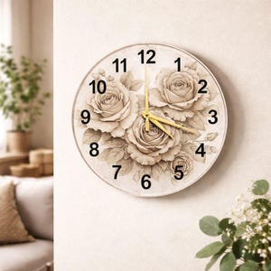 Könnte beinhalten: Runde Wanduhr mit einem floralen Rosendesign in Beige- und Cremetönen. Das Zifferblatt zeigt schwarze Ziffern und goldfarbene Zeiger. Die Uhr ist an einer neutralfarbenen Wand befestigt und verleiht jedem Raum einen Hauch von Eleganz. Durchmesser: ca. 30 cm.
