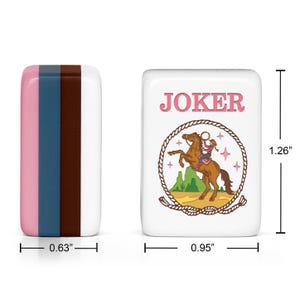 May include: Two rectangular mahjong tiles. The left tile features vertical stripes of pink, blue, and brown. The right tile is white with the word JOKER in pink above a graphic of a cowgirl on a horse inside a rope lasso. Dimensions are 1.26 inches by 0.95 inches by 0.63 inches.
