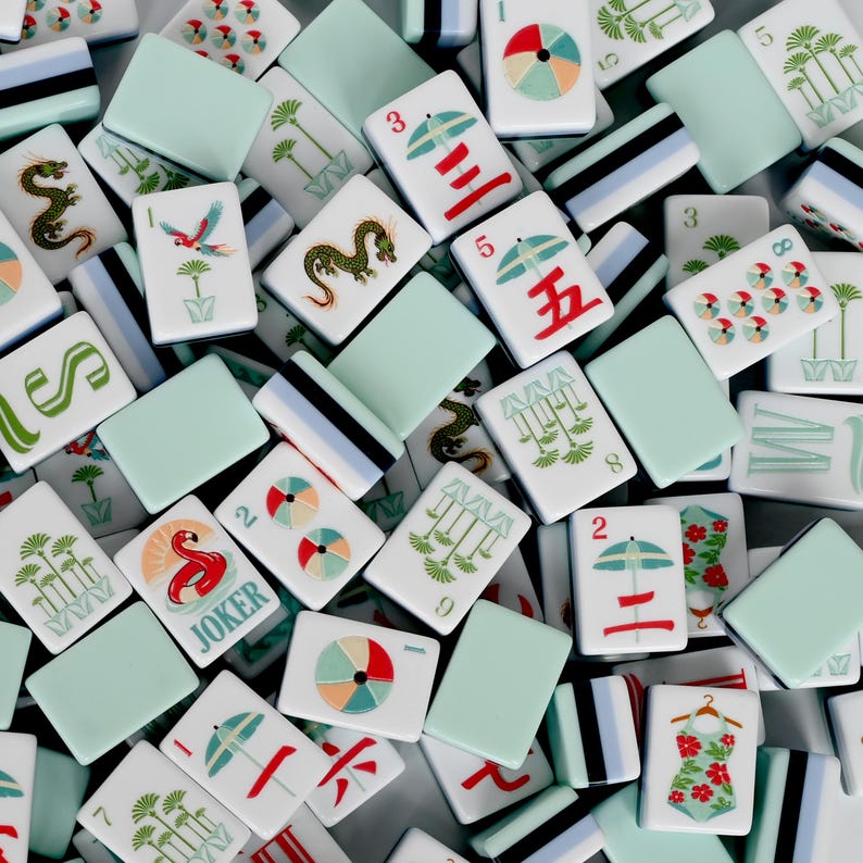 May include: A collection of rectangular mahjong tiles featuring a mix of solid light green backs and white faces with colorful illustrations. Designs include red umbrellas, green dragons, palm trees, a flamingo labeled JOKER, and floral swimsuits.