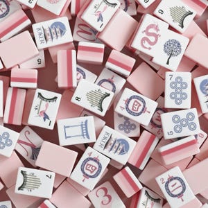 May include: A collection of rectangular mahjong tiles featuring a pastel pink and white color scheme. The tiles display various illustrations including a dragon, a tree, a pagoda, lanterns, and bamboo, alongside numerical and joker markings.