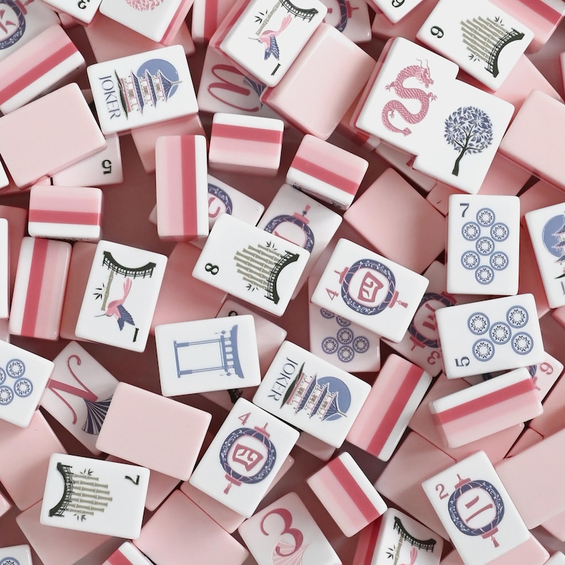 May include: A collection of rectangular mahjong tiles featuring a pastel pink and white color scheme. The tiles display various illustrations including a dragon, a tree, a pagoda, lanterns, and bamboo, alongside numerical and joker markings.