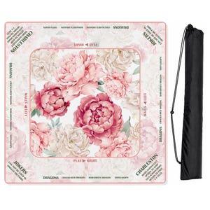May include: A square mahjong mat featuring a white background with large pink and cream peony flowers. The border includes text for game rules like Charleston, Jokers, and Dragons. A black drawstring storage bag is positioned to the right.