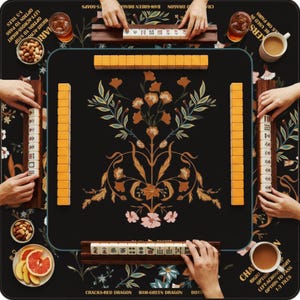 May include: A square mahjong mat with a black background featuring a central floral pattern in orange, pink, and green. The mat includes printed game instructions and is surrounded by four wooden tile racks holding ivory-colored mahjong tiles.