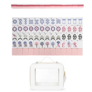May include: A set of white Mahjong tiles with pink backs, featuring various blue, pink, and black printed designs including numbers, dragons, flowers, and the letters N, E, W, S. The set includes a white rectangular carrying case with a clear window.