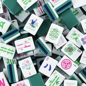 Puede incluir: Primer plano de una colecci&oacute;n de fichas de Mahjong blancas y verdes. Algunas fichas tienen rayas verdes y azules, mientras que otras presentan ilustraciones de flores, bamb&uacute; y caracteres. La palabra "JOKER" es visible.