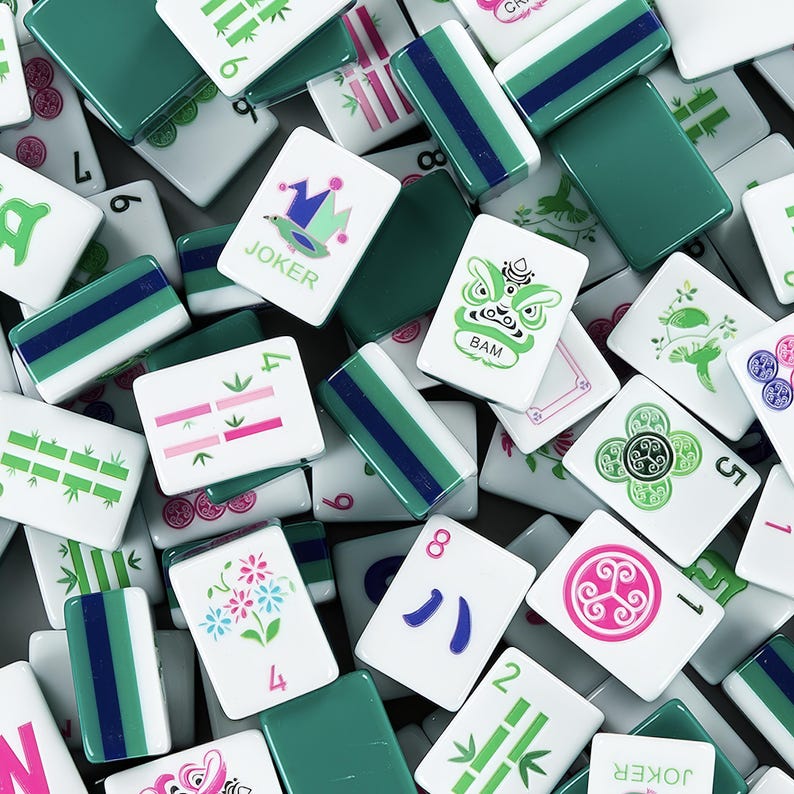 Puede incluir: Primer plano de una colecci&oacute;n de fichas de Mahjong blancas y verdes. Algunas fichas tienen rayas verdes y azules, mientras que otras presentan ilustraciones de flores, bamb&uacute; y caracteres. La palabra "JOKER" es visible.