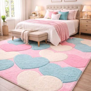 May include: A bedroom scene featuring a large pink rug with heart-shaped designs in light blue and off-white. The room includes a bed with pink and white bedding, a bench, and two framed floral prints on the wall. The room is well-lit with natural light.
