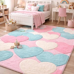 May include: A pink, blue, and white heart-shaped rug in a bedroom setting. The rug features large, fluffy hearts in varying shades of pink, blue, and white. The room includes a white bed, desk, and other decor.