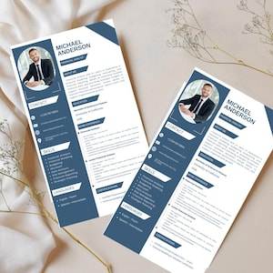 May include: Two resumes with a photo of a smiling man in a suit, labeled "Michael Anderson." The resumes have a blue and white design, listing contact information, skills, and experience. The resumes are on a beige surface with decorative sprigs.