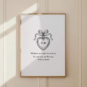 A framed print with a wooden frame. The print features a heart-shaped design with the initials "C+H" inside, adorned with a bow and ribbon. Below the design is a quote from Wuthering Heights.